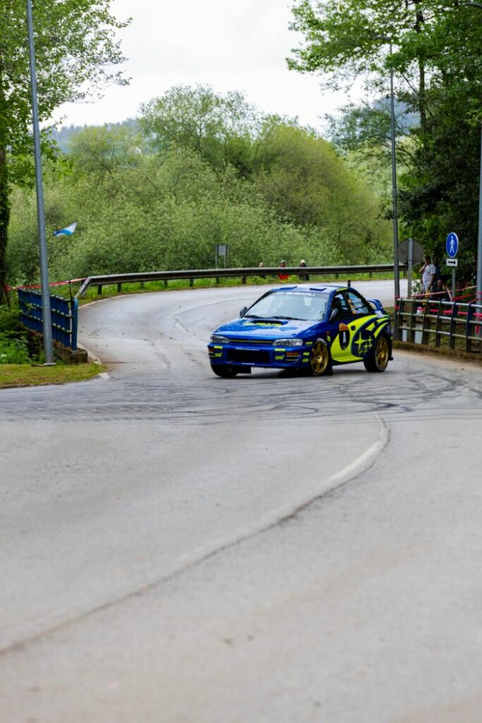 Rally car speeding along a curvy road in a scenic outdoor setting, showcasing motorsport excitement.